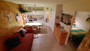 Een gezellige, compacte ruimte met een houten wand, een rode bank, een eettafel en een kitchenette.