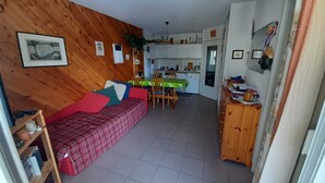 Een gezellige kamer met een rode geruite bank, een eettafel met stoelen en een keukenhoek met kastjes en een spoelbak.