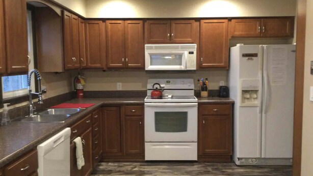 A kitchen with wooden cabinets, a white microwave, a stove, and a refrigerator. - 5 Star Location (Springfield)