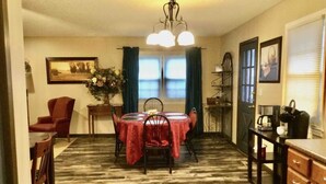 A dining area with a round table covered in a red tablecloth, surrounded by chairs. There is a chandelier above the table, and a window with curtains to the left. - 5 Star Location (Springfield)