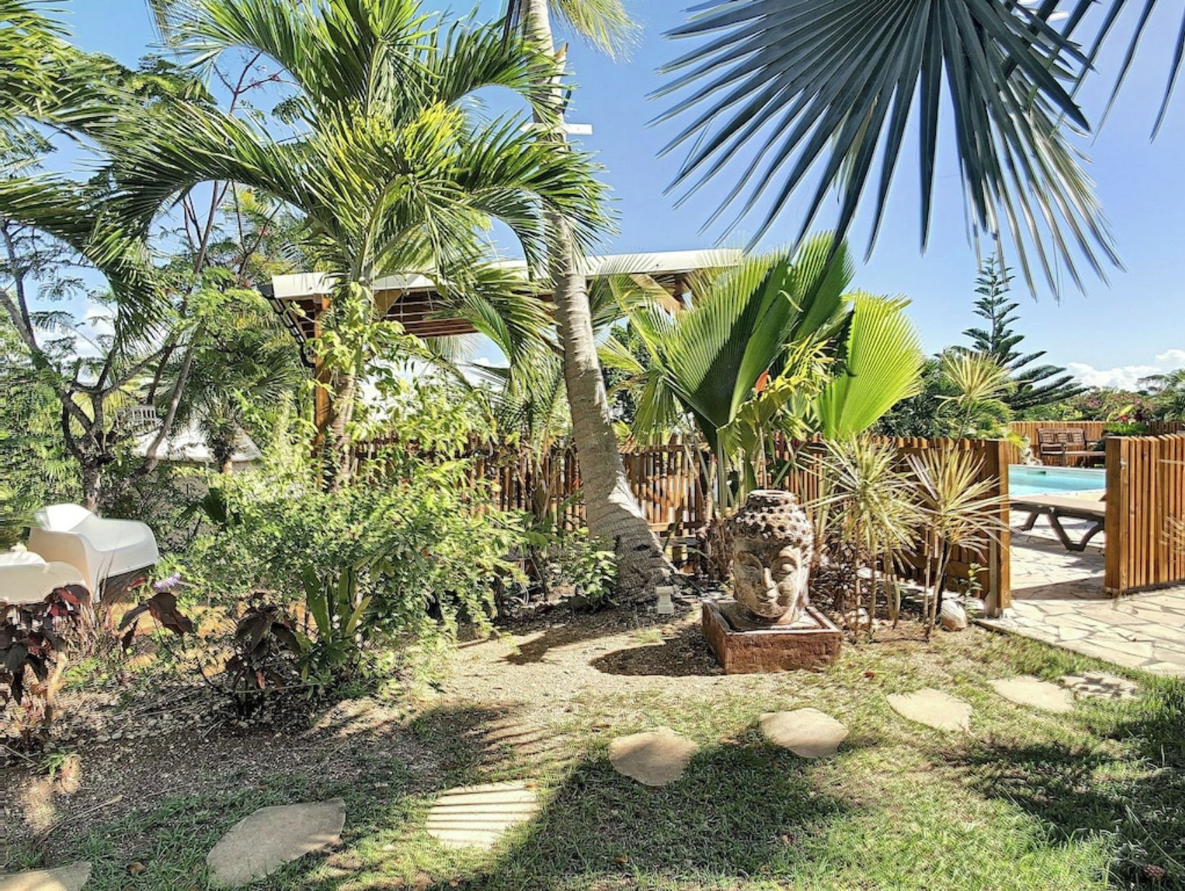 A tropical garden with palm trees, a statue, and a wooden fence.