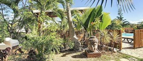 A tropical garden with palm trees, a statue, and a wooden fence.