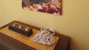 A framed floral artwork of roses on a yellow wall, a candle holder with three candles, and a woven basket on a wooden table. - Eckhorst Farm, Ruhwinkel (Güby)