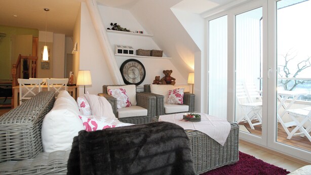 A cozy living room with wicker furniture, a clock, and a view of the outside balcony. - Eckhorst Farm, Ruhwinkel (Güby)
