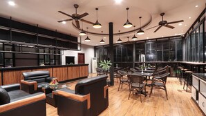 A modern kitchen with dark cabinetry, a central island, and a seating area with sofas and chairs. - The Garden Park by Lucky Courtyard (Siem Reap)