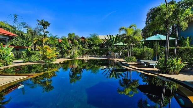 A clear pool surrounded by lush greenery and palm trees, with lounge chairs and umbrellas. - The Garden Park by Lucky Courtyard (Siem Reap)