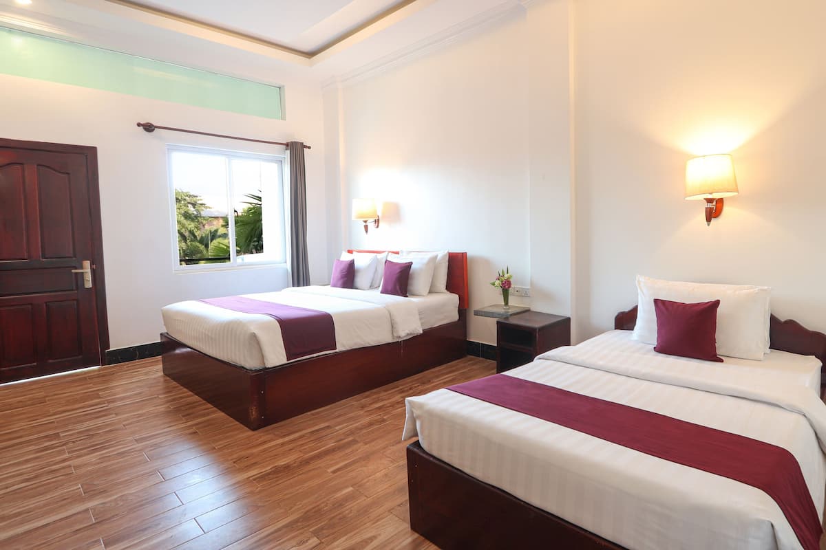 A hotel room with two beds, wooden flooring, a window with curtains, and wall-mounted lamps.
