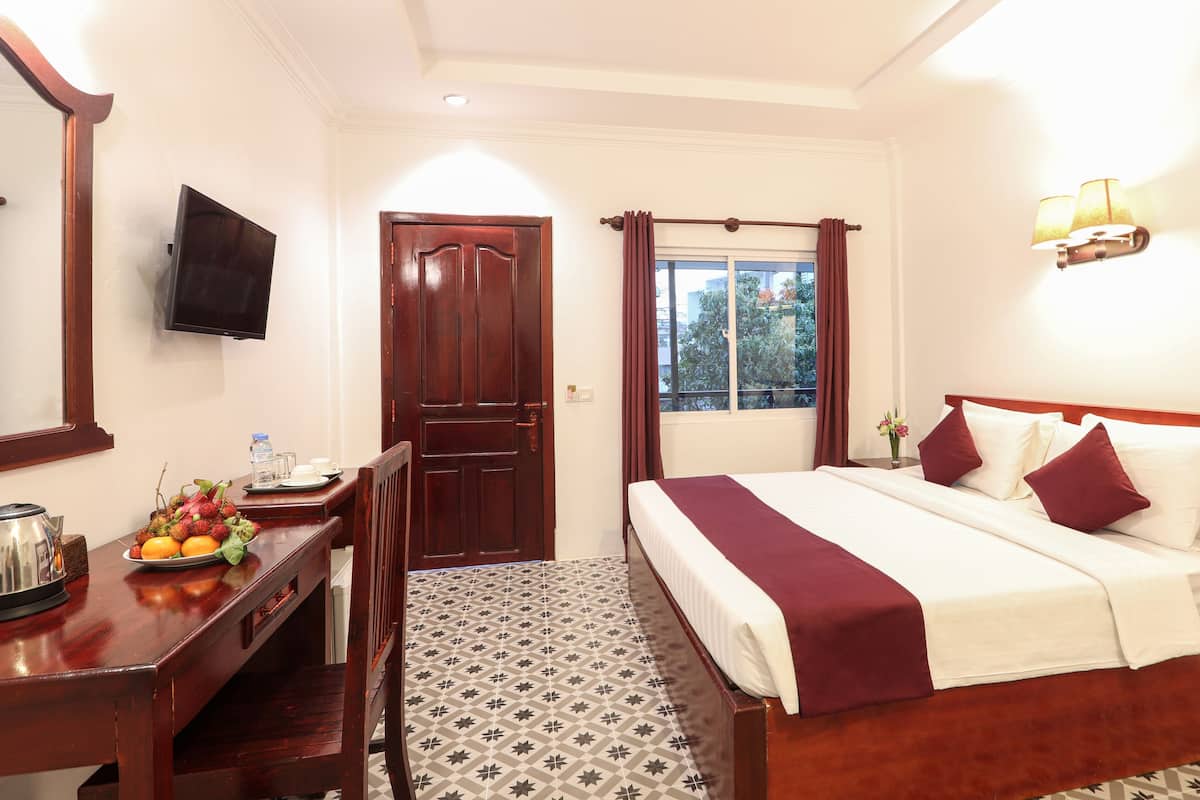 A hotel room with a bed, a desk with a fruit bowl, a TV, and a window with curtains.