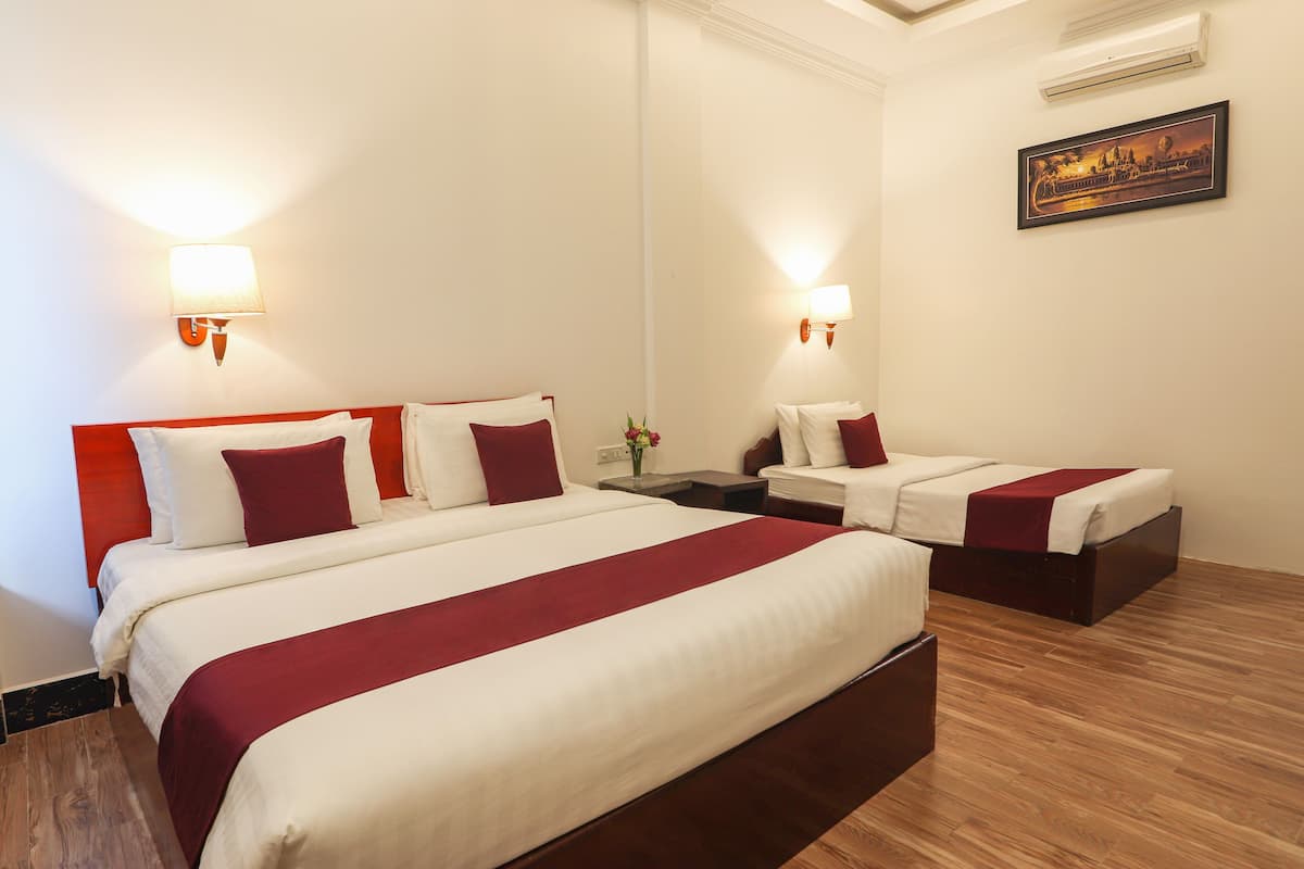 A hotel room with two beds, each with white and red bedding, a nightstand with a vase of flowers, and a framed picture on the wall.