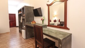 A compact room with a wooden desk, a chair, a small refrigerator, a flat-screen TV, and a mirror. - The Garden Park by Lucky Courtyard (Siem Reap)