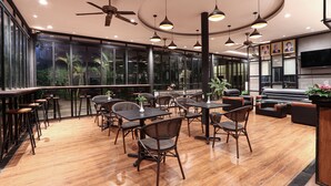 A modern dining area with wooden flooring, black and brown furniture, and large windows offering views of greenery. - The Garden Park by Lucky Courtyard (Siem Reap)