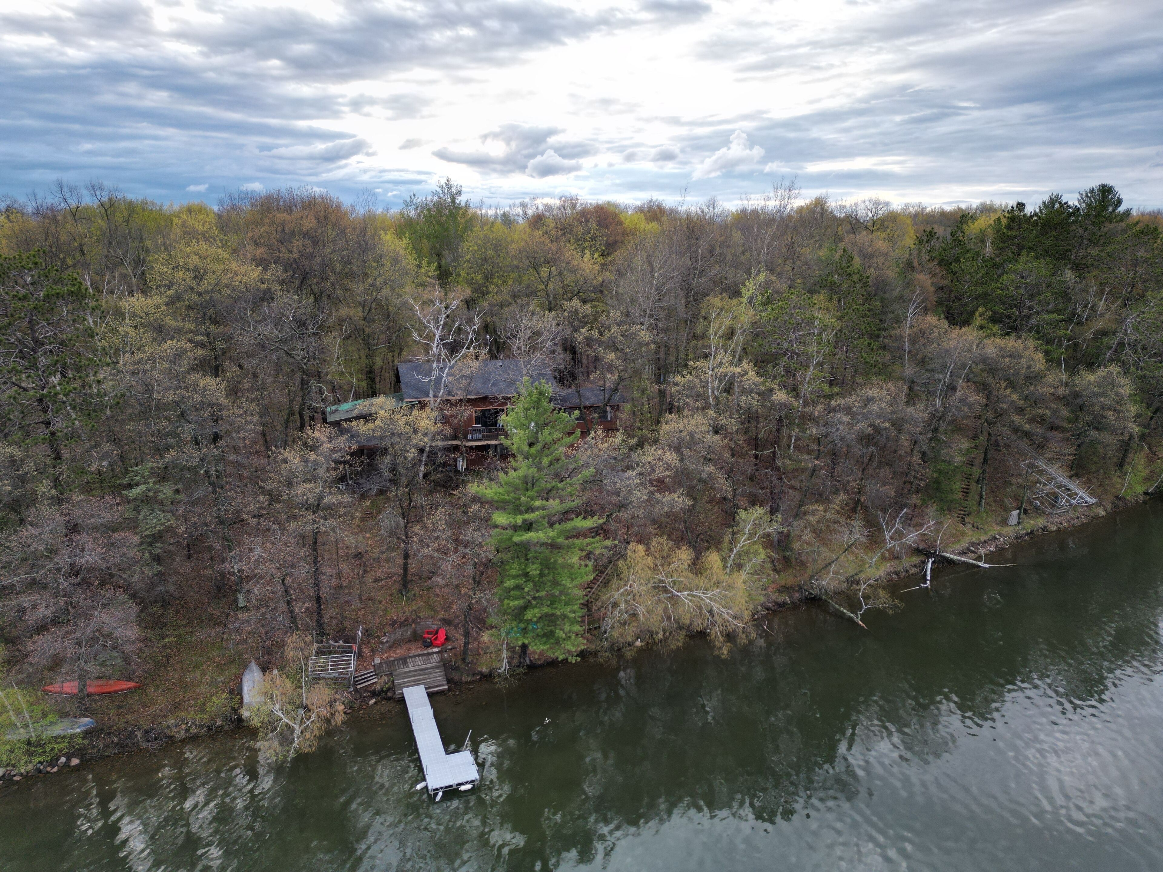 A cabin surrounded by dense forest, a dock extending into a river, and a cloudy sky.