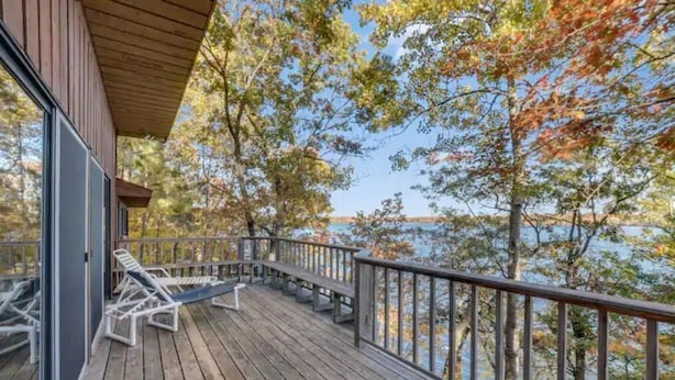 Terraza de madera con sillones de descanso con vista a un lago, rodeada de árboles.