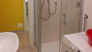 Un baño con ducha envuelta en vidrio, inodoro blanco y lavadora.