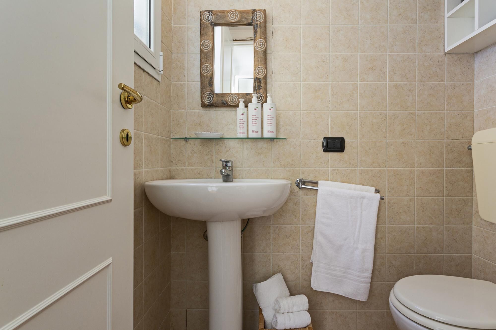 A bathroom with a white sink, a glass shelf with toiletries, a towel rack, and a toilet.