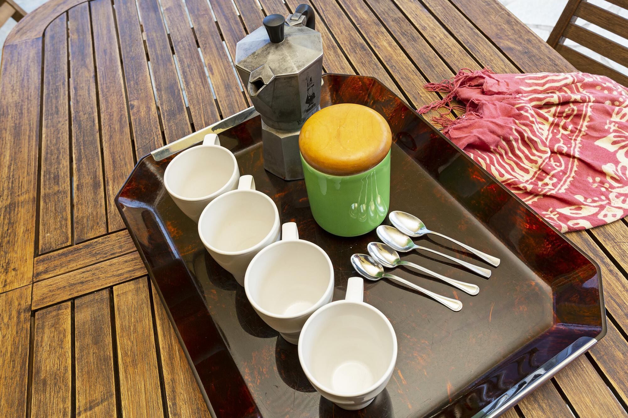 A tray with four white cups, a green mug, and several spoons on a wooden table.