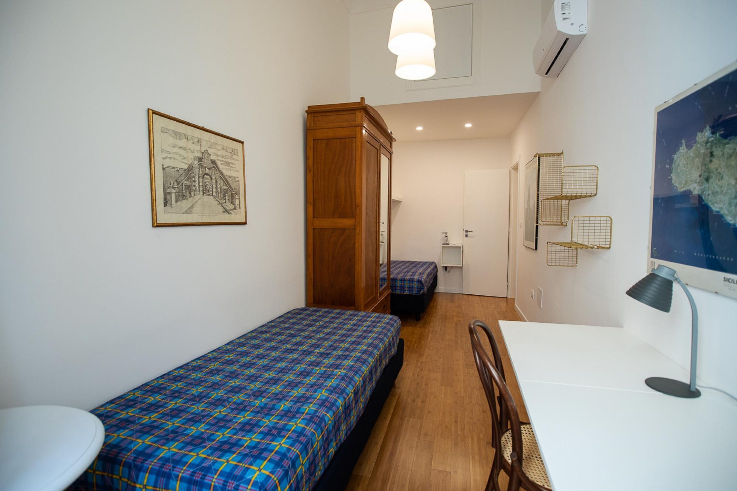 A small, clean room with two single beds, a wooden wardrobe, a desk, and a chair.