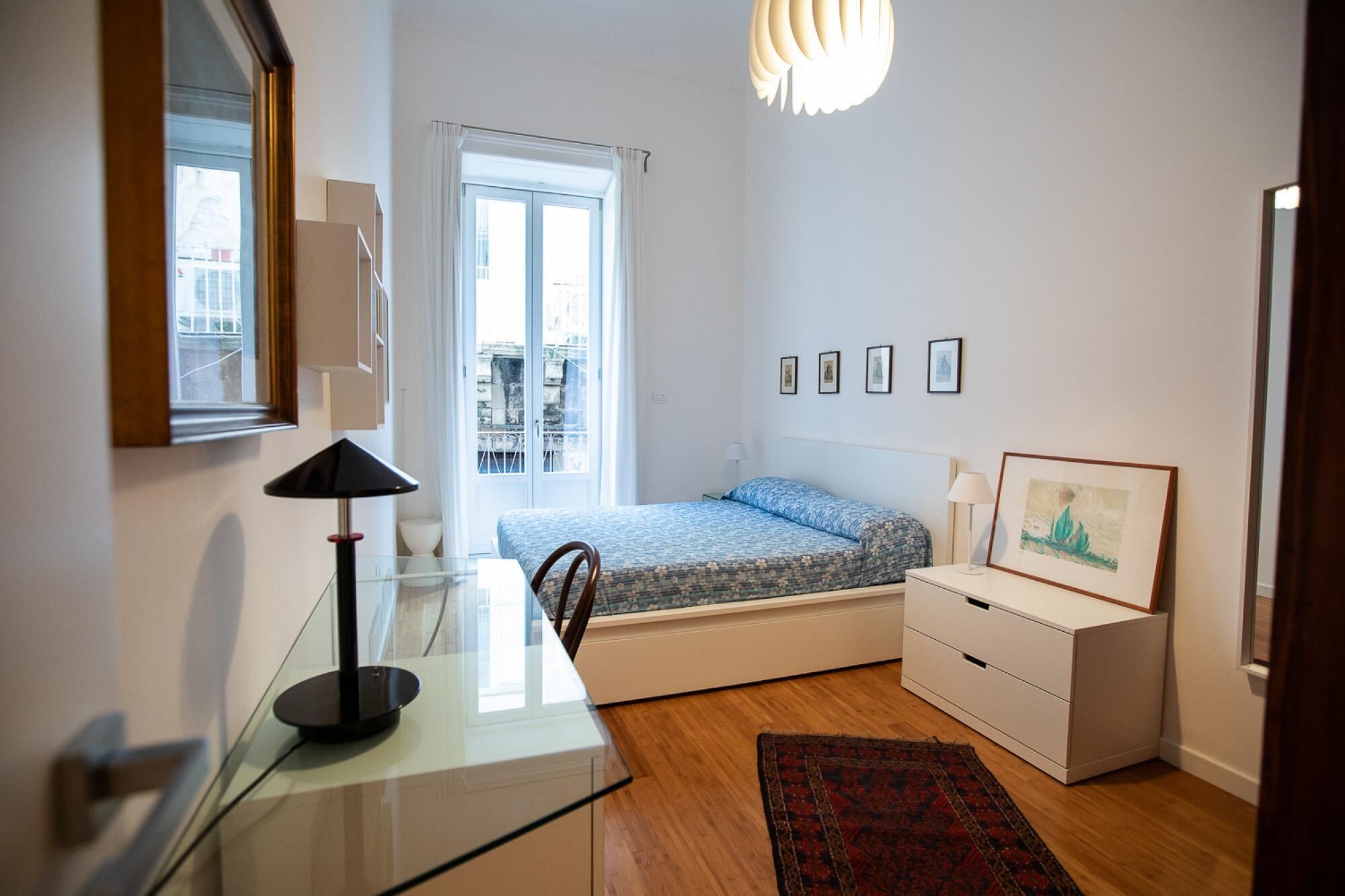 Un dormitorio con cama, mesita de noche, lámpara y vistas a la ciudad a través de una ventana.