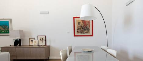 Un comedor con una mesa, sillas, una lámpara y obras de arte enmarcadas en la pared.