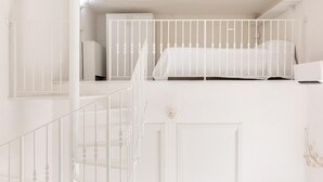 A white room with a bed, a desk, and a staircase. - Studio Dione 130 by Wonderful Italy (Syracuse)
