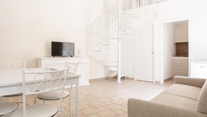 A spacious living area with a white staircase, a dining table with chairs, a sofa, and a television on a white cabinet. - Studio Dione 130 by Wonderful Italy (Syracuse)