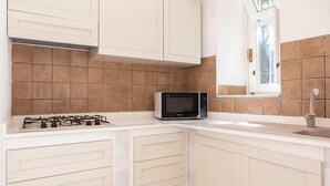 A kitchen with white cabinets, a gas stove, a microwave, and a window with a view of greenery. - Studio Dione 130 by Wonderful Italy (Syracuse)