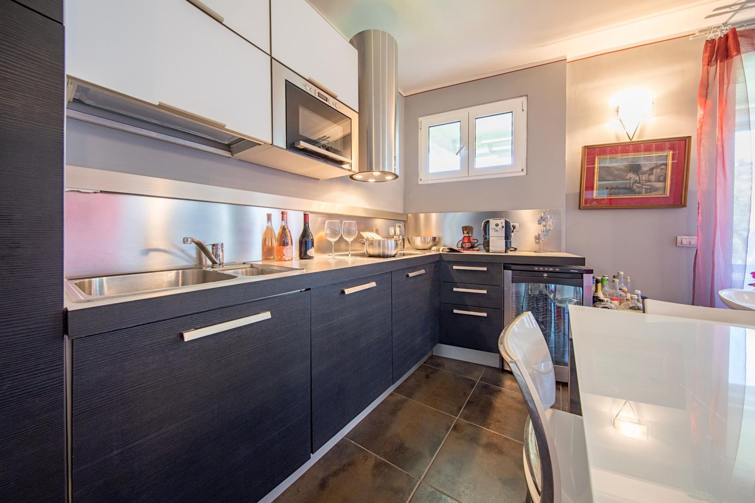 A modern kitchen with dark cabinetry, stainless steel appliances, and a large window.