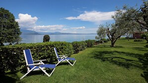 A grassy area with two blue lounge chairs facing a body of water and distant mountains. - San Sivino 55 con Piscina by Wonderful Italy (Manerba del Garda)