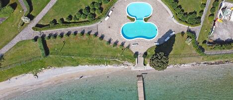 Vista aérea de un complejo turístico con una piscina central grande, una zona de playa y un muelle que se adentra en el agua.