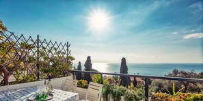 A terrace with a table set for dining, overlooking a coastal view with the sea and trees. - Una Terrazza sul Golfo di Ospedaletti by Wonderful Italy (Ospedaletti)