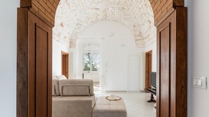 A room with a wooden door frame, a beige sofa, a television, and a tiled floor. - Villa Tranquillo 1876 by Wonderful Italy (Ostuni)