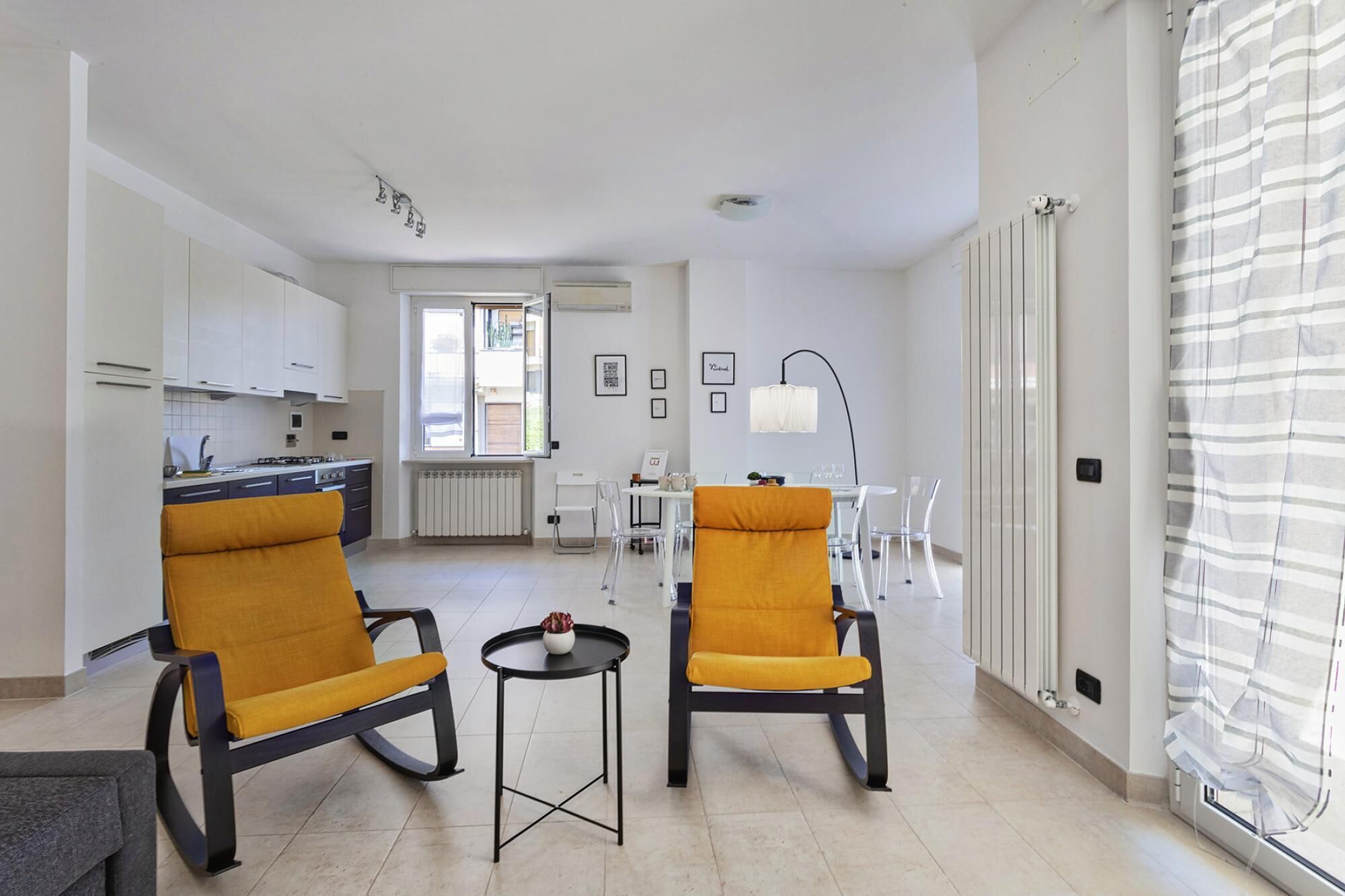 Un salon moderne avec deux fauteuils jaunes, une petite table et une cuisine en arrière-plan.