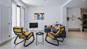Ein modernes Wohnzimmer mit einer Couch, zwei Schaukelstühlen, einem Fernseher und einem Gemälde an der Wand.