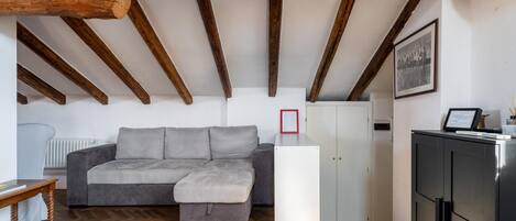 A loft-style room with exposed wooden beams, a grey sectional sofa, a white cabinet, and a radiator.