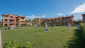A courtyard with a grassy lawn, outdoor seating, and a building with balconies. - Baglio Degli Ulivi 3 by Wonderful Italy (Sirmione)