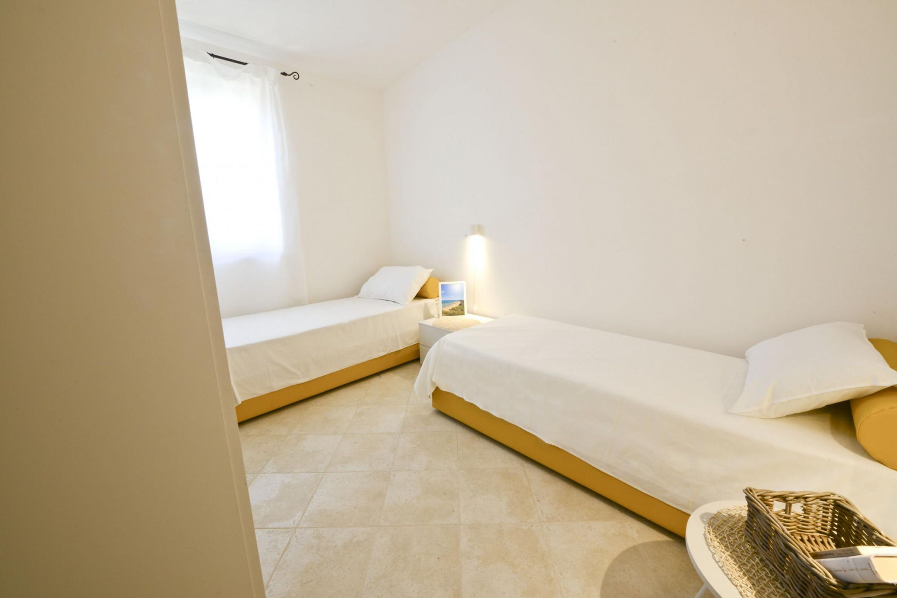 Een kleine, schone kamer met twee eenpersoonsbedden, een nachtkastje met een lamp en een raam met gordijnen.
