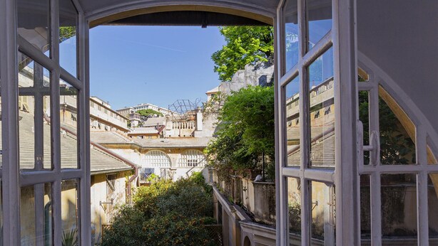 Blick durch ein Fenster auf ein Mehrstöckiges Gebäude mit Balkonen und einem Innenhof mit viel Grün.