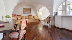 Ein geräumiges Wohnzimmer mit Holzboden, einer Sofagarnitur, einem Esstisch mit Stühlen und einem großen Bogenfenster.