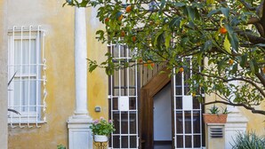 Ein gelbes Gebäude mit einer weißen Säule, einem Fenster mit Metallgitter und einem Blumentopf auf dem Boden.