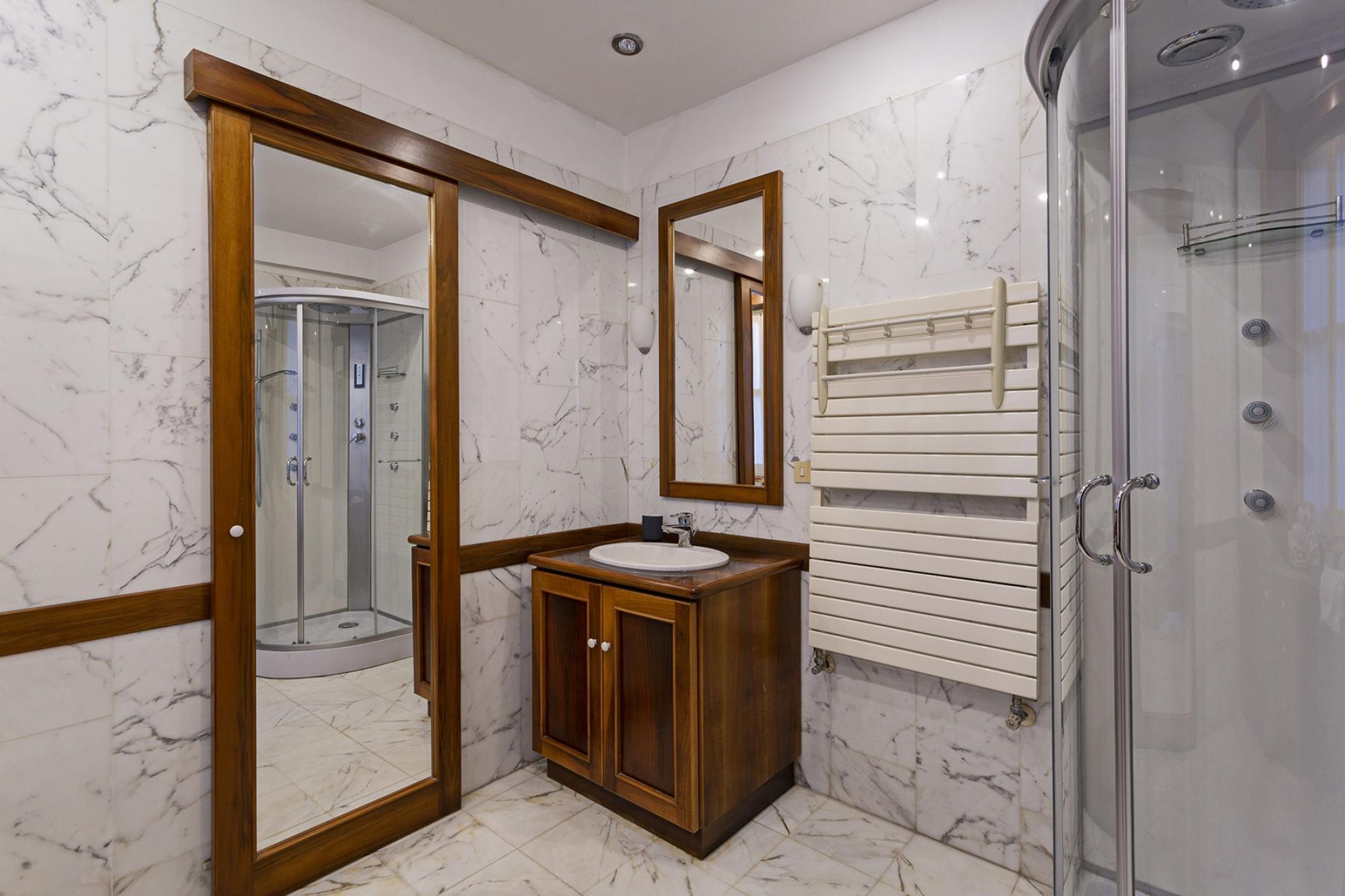 Une salle de bain moderne avec un sol en marbre, un meuble-lavabo en bois, une cabine de douche en verre et un porte-serviettes.