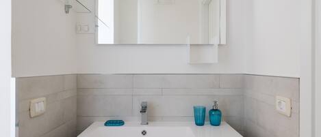 A bathroom with a white sink, a mirror, and a glass shelf.