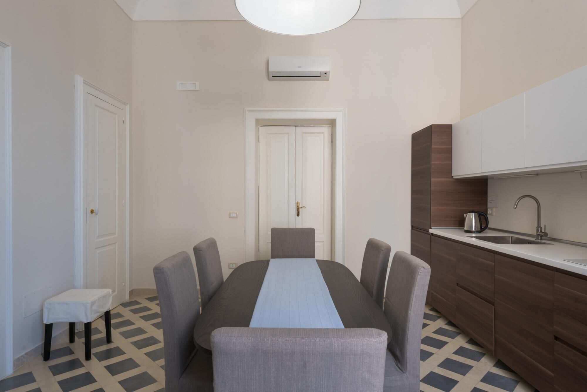 A compact kitchen with a dining table, chairs, a small stool, and a built-in oven.