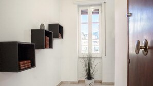 A hallway with a potted plant, a window with blinds, and a door. - Casa Aglian con Vista by Wonderful Italy (Cefalù)
