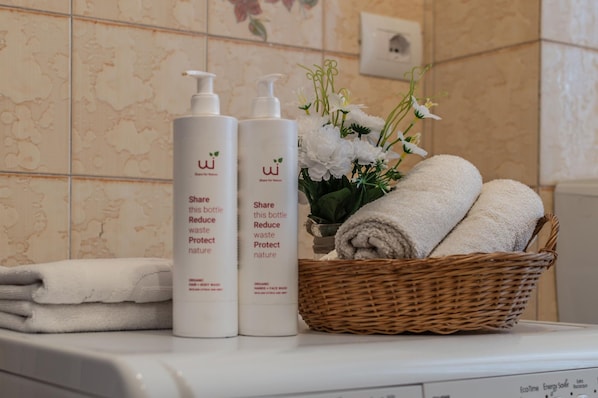 A bathroom with two bottles of shampoo, a basket of towels, and a vase of flowers.