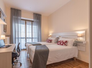Une chambre d’hôtel avec deux lits, un bureau avec un ordinateur portable, une chaise et une fenêtre avec des rideaux.