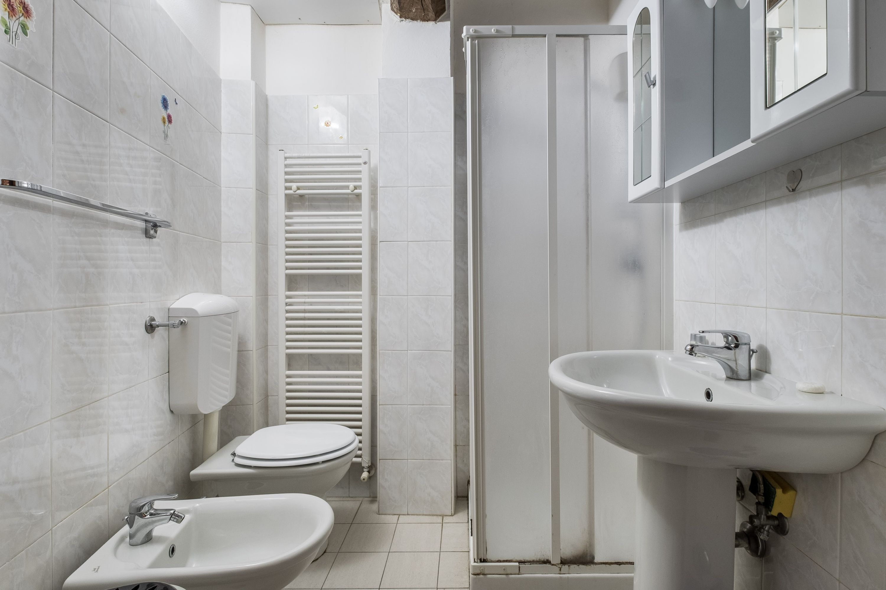 A modern bathroom with a toilet, bidet, sink, and a towel rack.