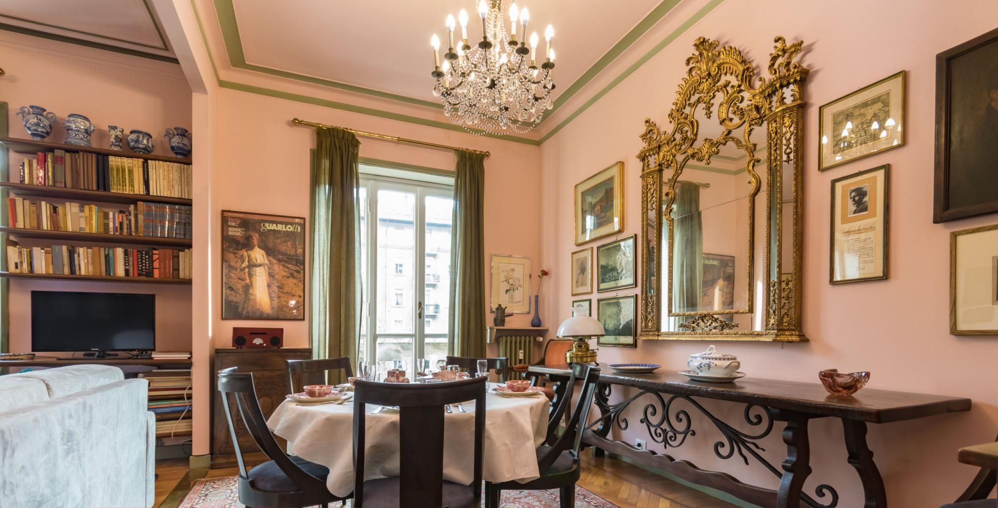 Un coin repas avec une table dressée pour quatre personnes, entourée de chaises, d’un lustre et d’une bibliothèque remplie de livres.