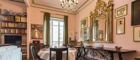 Un coin repas avec une table dressée pour quatre personnes, entourée de chaises, d’un lustre et d’une bibliothèque remplie de livres.
