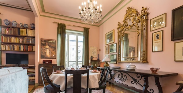 Un coin repas avec une table dressée pour quatre personnes, entourée de chaises, d’un lustre et d’une bibliothèque remplie de livres.