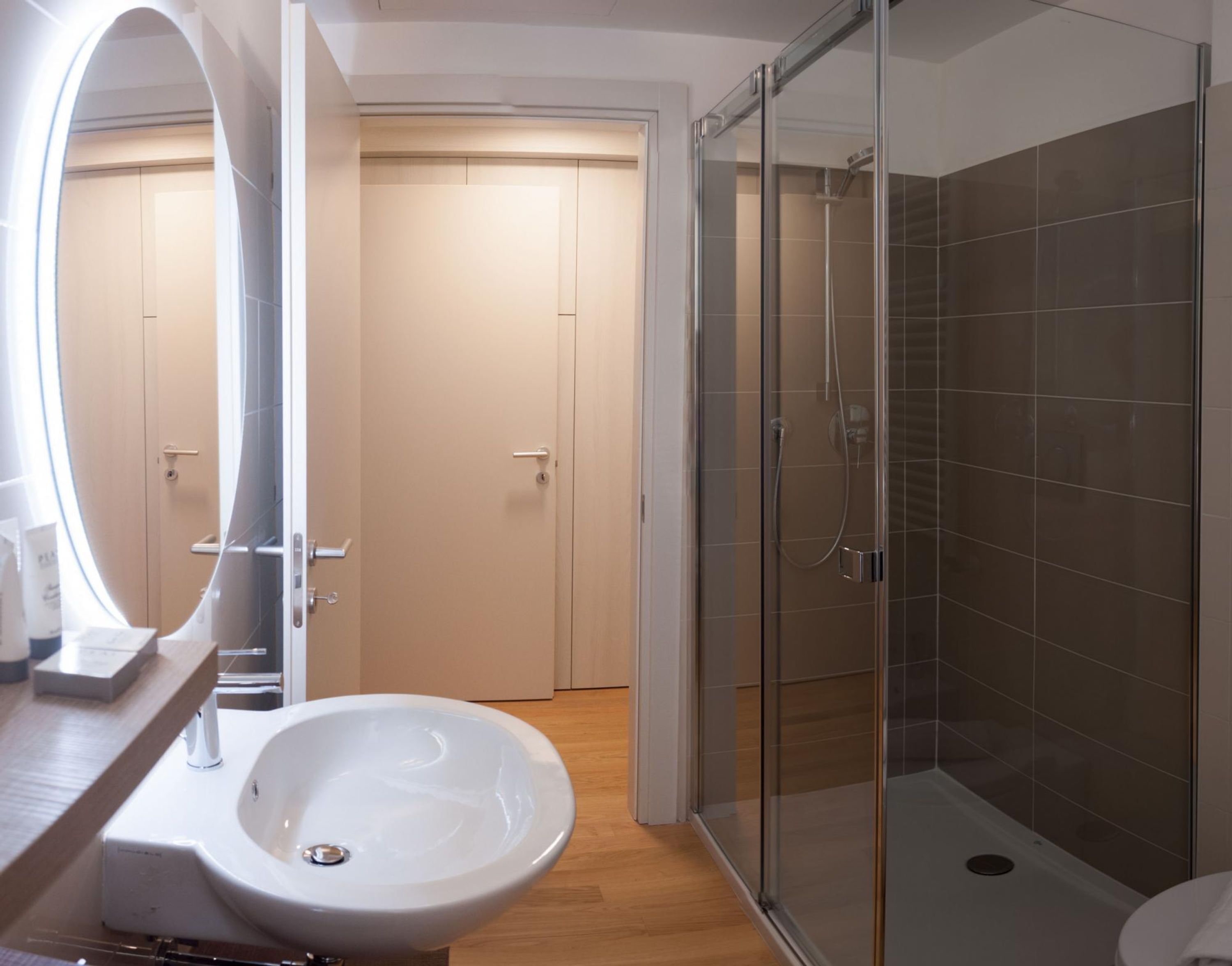 Une salle de bain moderne avec un grand lavabo ovale, une douche en verre et une porte donnant sur une autre pièce.